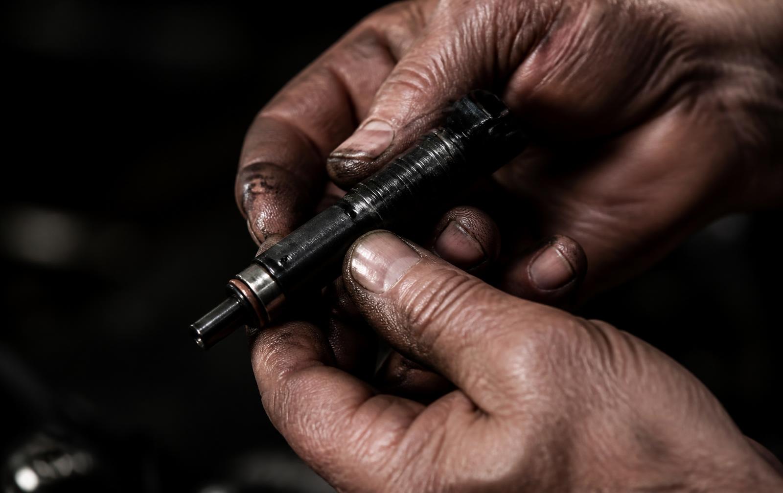 The hands of a senior automotive engineer holding a fuel injector in a dark workshop